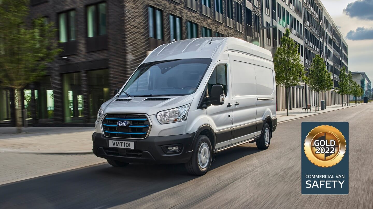 Ford E-Transit z částečného pohledu zepředu, jedoucí po městské ulici, s oceněním Gold 2022 Commercial Van Safety.