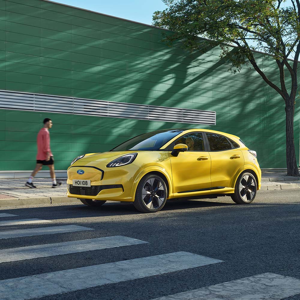 A yellow Ford Puma Gen-E parked by the side of the road.