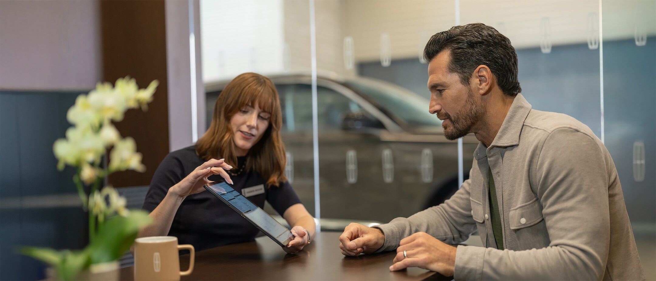 Žena ukazuje Ford Protect záruku na tabletu muži v autosalonu.