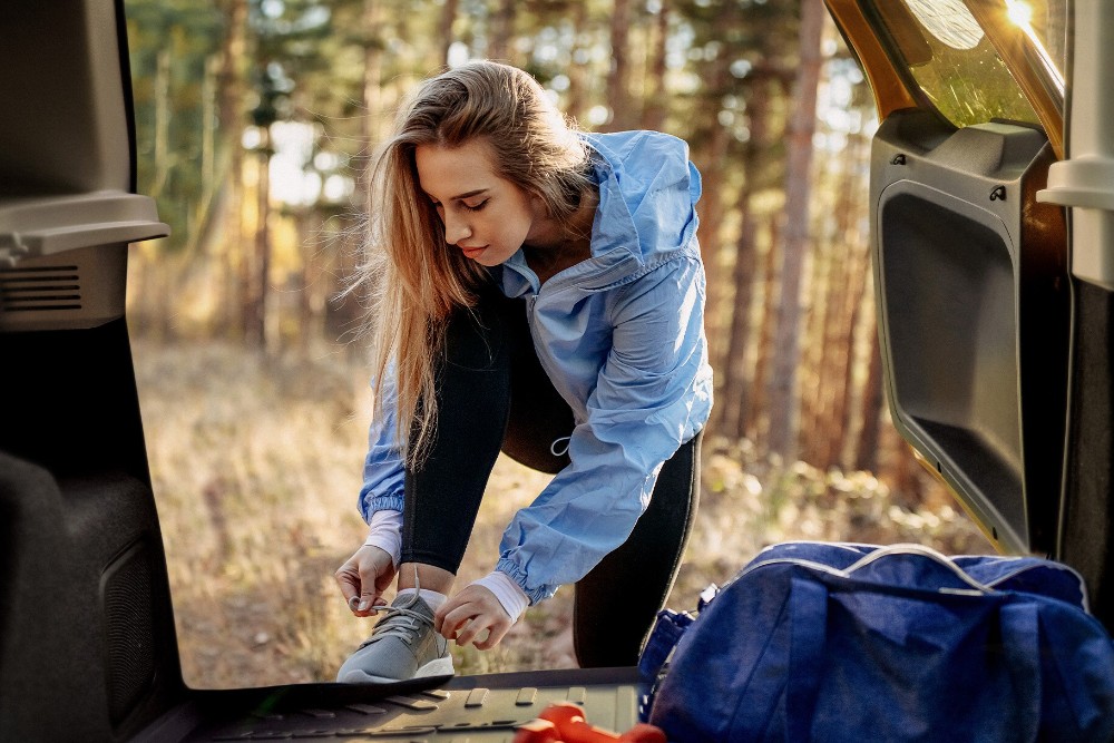 Žena si zavazuje boty ve dveřích vozu značky Ford