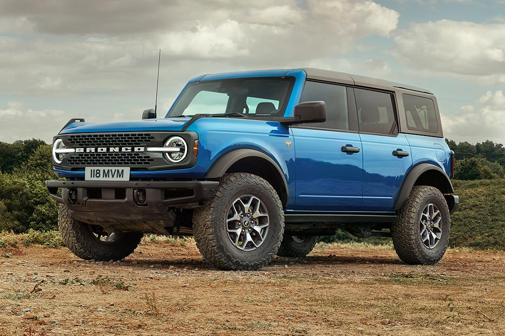 Čelní tříčtvrteční pohled na modrý Ford Bronco zaparkovaný na polní cestě.