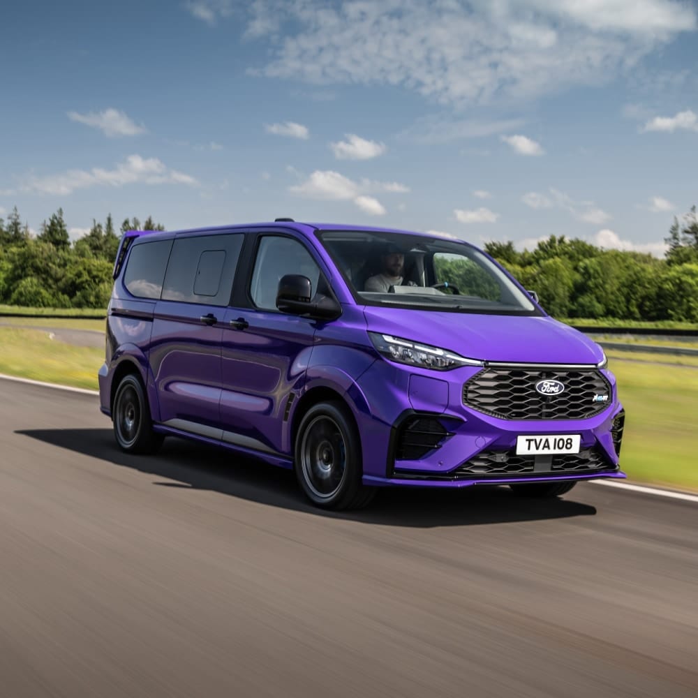 Fialový Ford Tourneo Custom jedoucí po silnici, s osobou viditelnou na sedadle řidiče