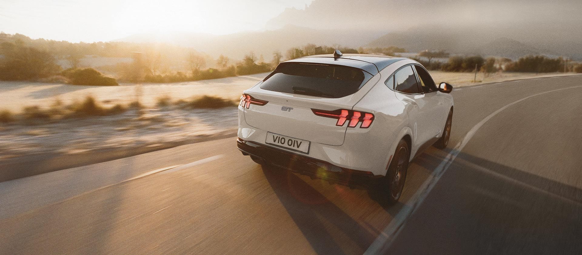 Stříbrný elektromobil Ford Mustang Mach-E jedoucí po dlouhé otevřené silnici.