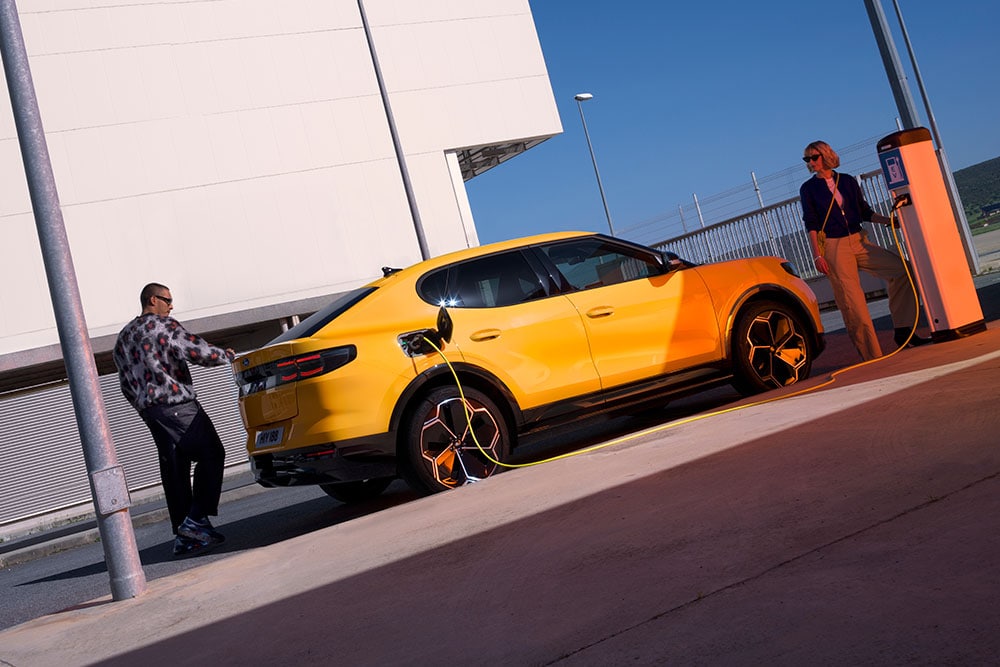Lidé nabíjející žlutý Ford Capri na veřejné nabíjecí stanici.