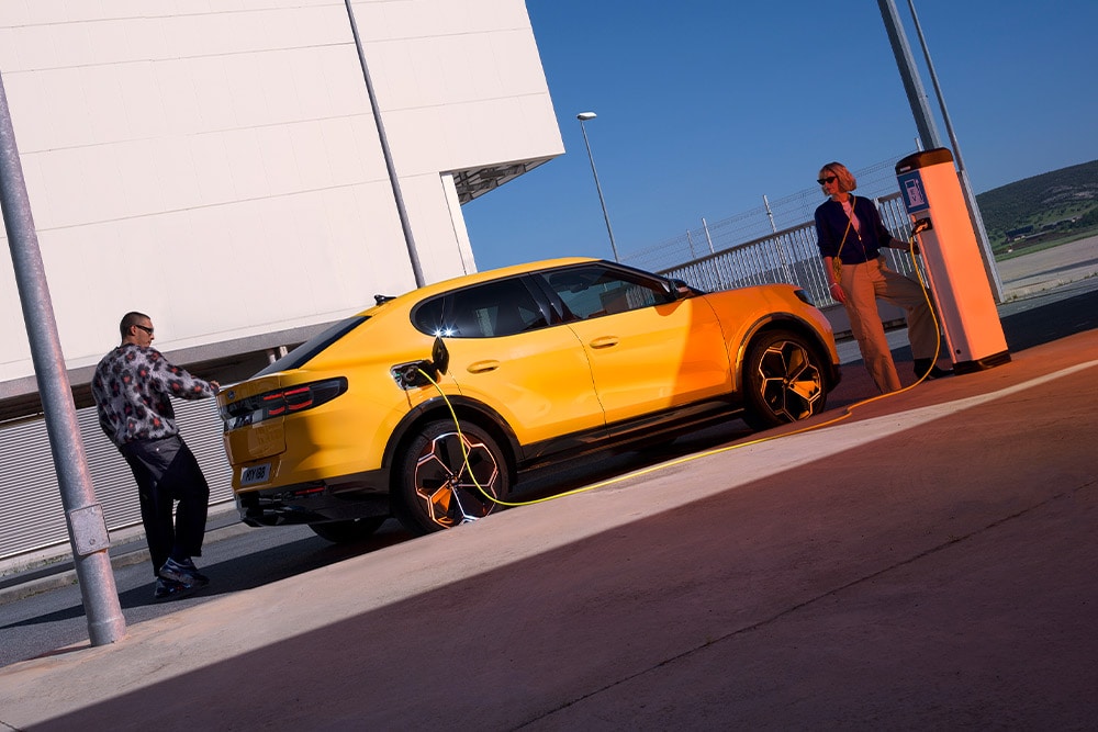 Lidé nabíjející žlutý Ford Capri EV u veřejné nabíjecí stanice.