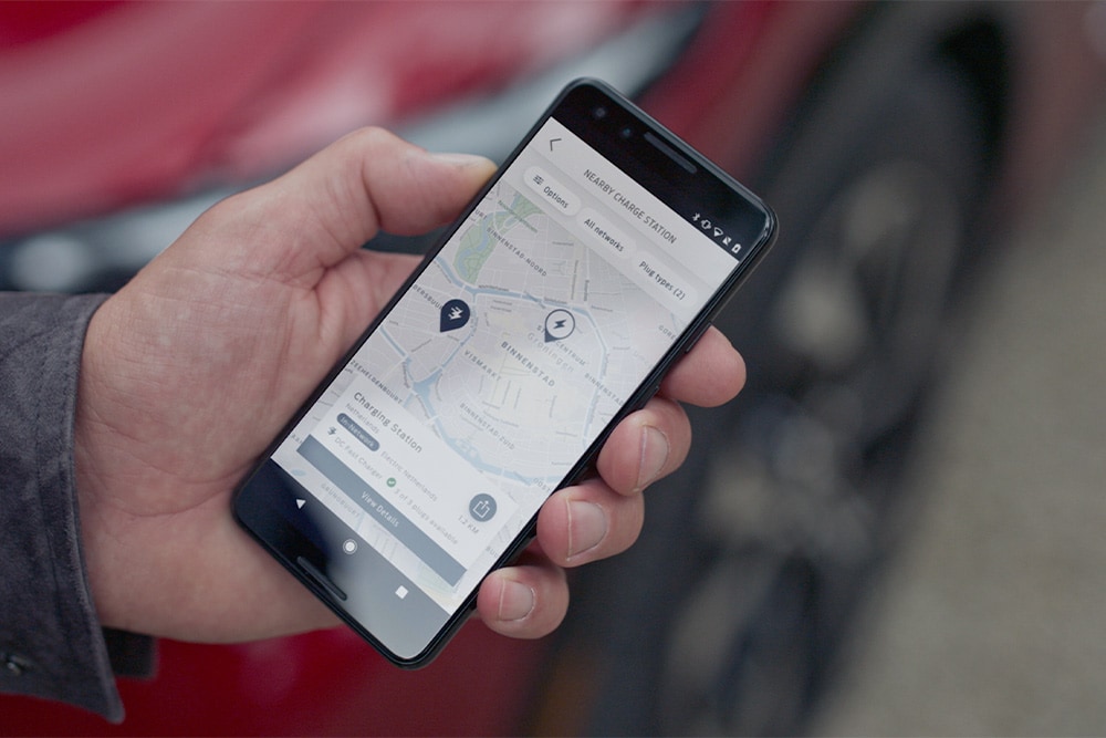 Chytrý telefon zobrazující aplikaci FordPass™ s blízkými nabíjecími místy pro veřejné nabíjení elektromobilů Ford.