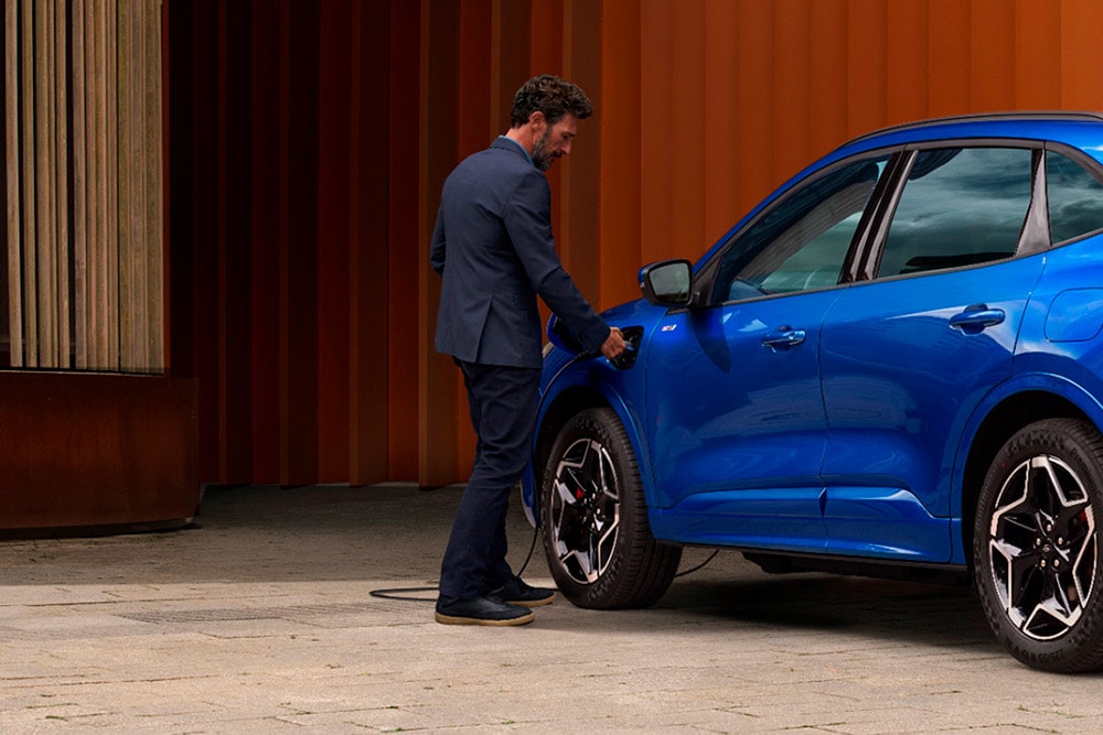 Osoba připojující kabel pro domácí nabíjení elektromobilu k hybridnímu vozu Ford.