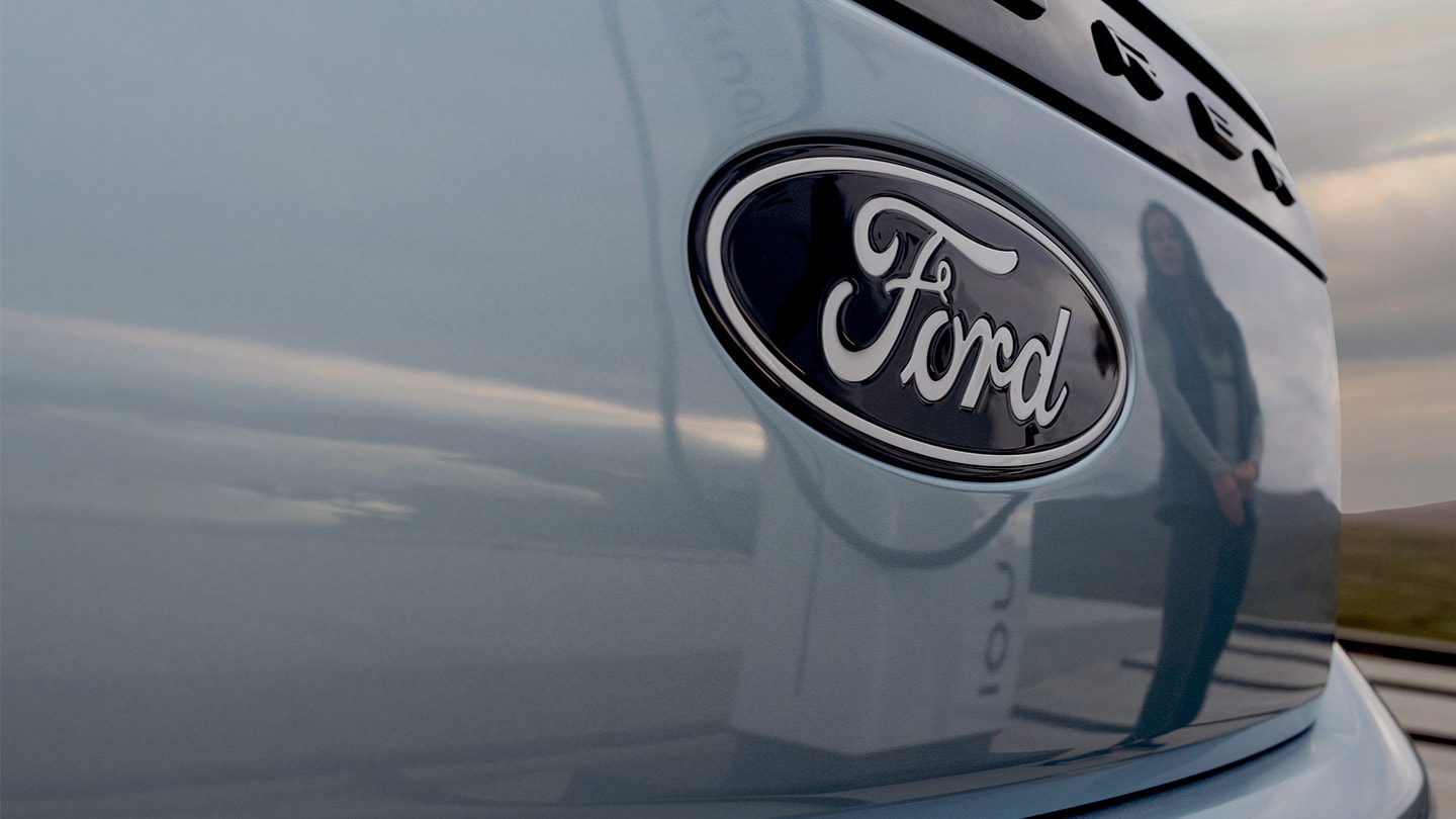 Logo Ford na modrém elektromobilu Ford Explorer s odrazem veřejné nabíjecí stanice.