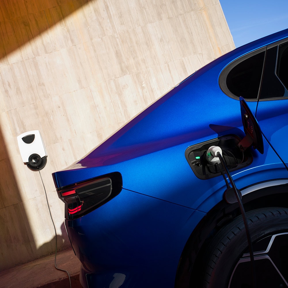 Pohled zezadu na modrý elektromobil Ford Capri připojený k domácímu nabíjecímu místu pro elektromobily.