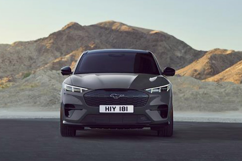 Čelní pohled na černý Ford Mustang Mach-E zaparkovaný před hornatou krajinou.