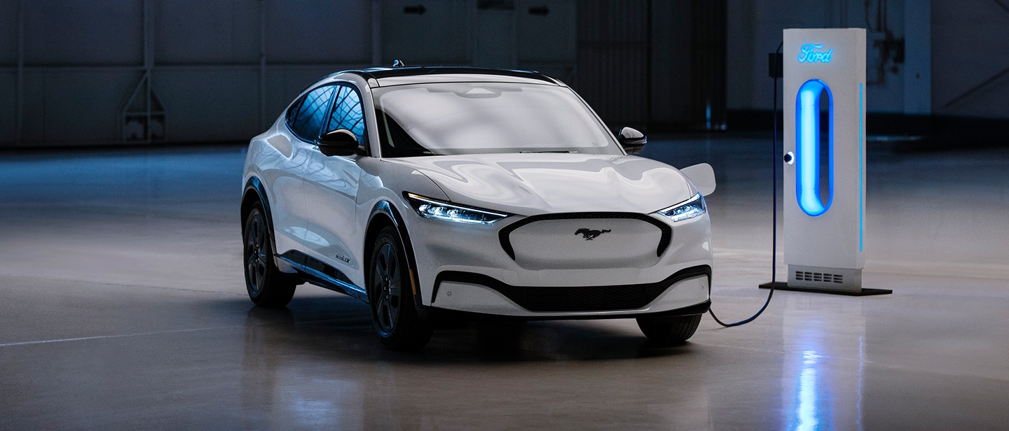 A white Ford Mustang Mach-E parked in a garage, connected to a glowing blue charging station.