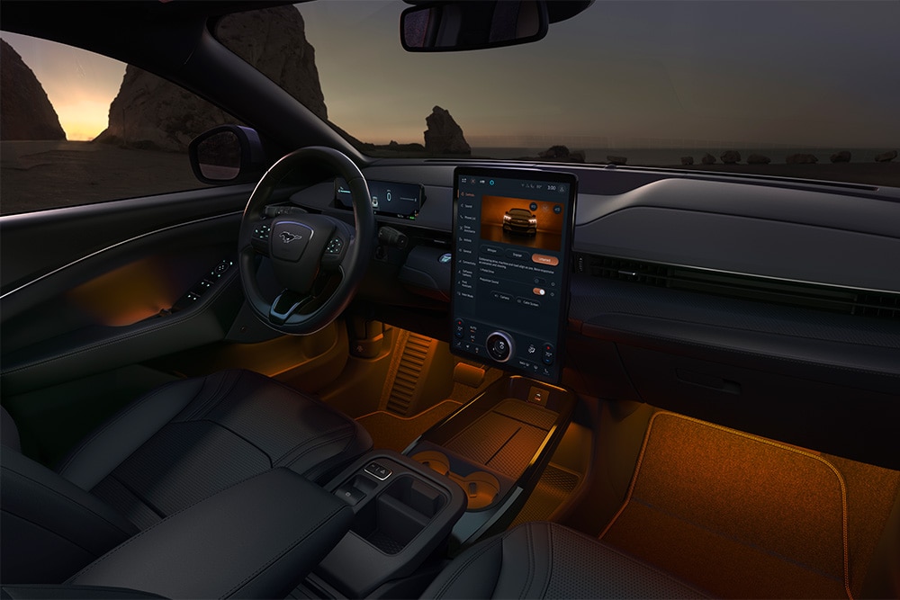 Noční záběr na interiér Fordu Mustang Mach-E s 15,5" dotykovou obrazovkou SYNC 4 a ambientním LED osvětlením nastaveným na oranžovou barvu