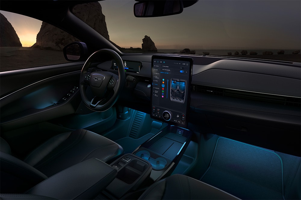 Noční záběr na interiér Fordu Mustang Mach-E s 15,5" dotykovou obrazovkou SYNC 4 a ambientním LED osvětlením nastaveným na modrou barvu