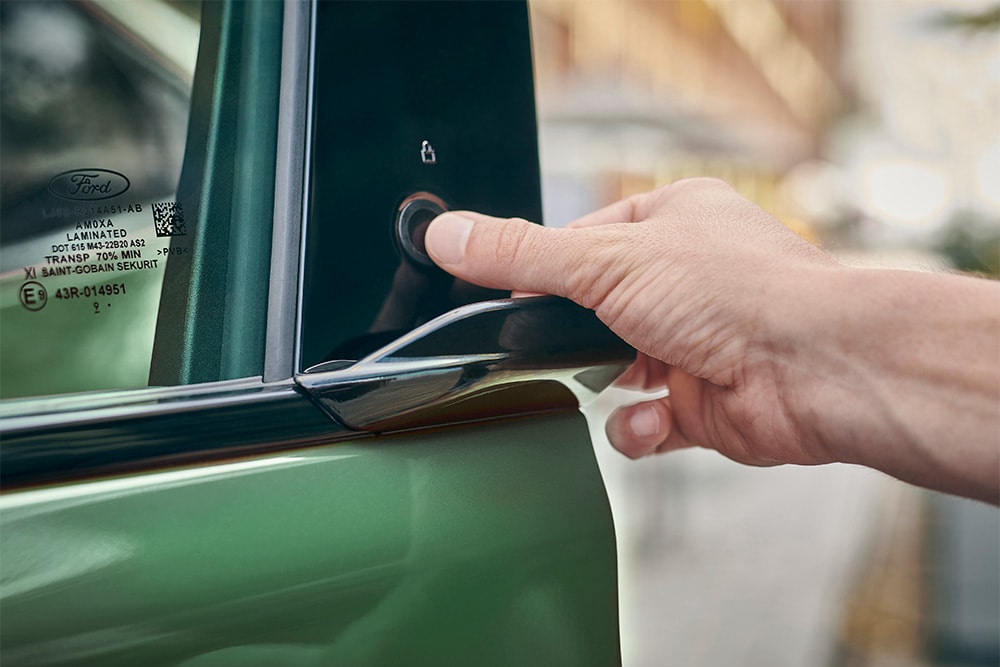 Detailní záběr na ruku ovládající systém E-Latch stisknutím tlačítka na dveřích zeleného Fordu Mustang Mach-E.