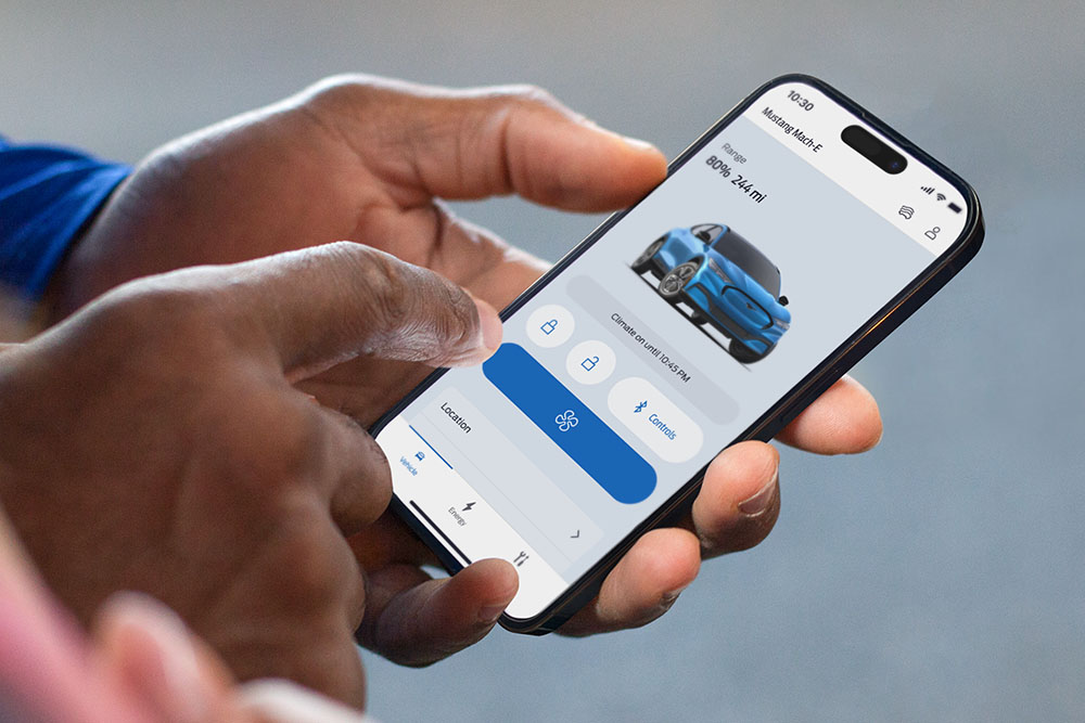 Detailní záběr na iPhone zobrazující aplikaci FordPass s grafikou Ford Mustang Mach-E a několika tlačítky aplikace.