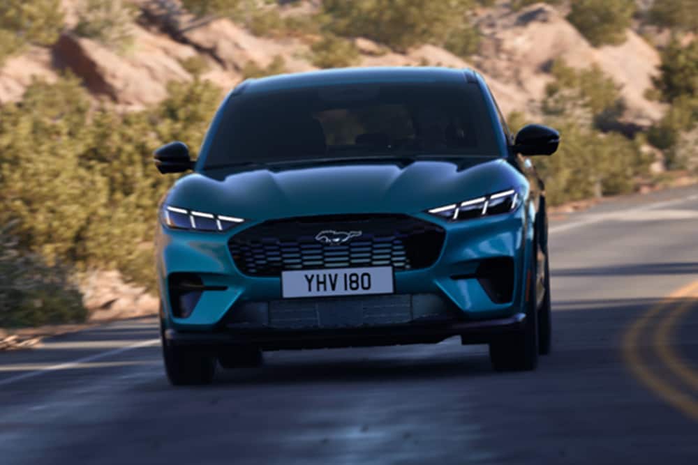 Čelní záběr na modrý Ford Mustang Mach-E jedoucí po horské silnici.