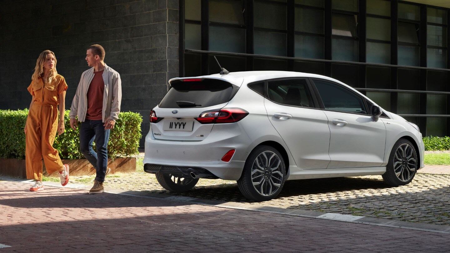 Ford Fiesta tříčtvrteční pohled zezadu se dvěma osobami vedle vozu