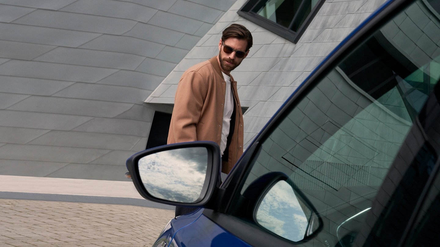 Closeup of a door mirror with a man standing behind it