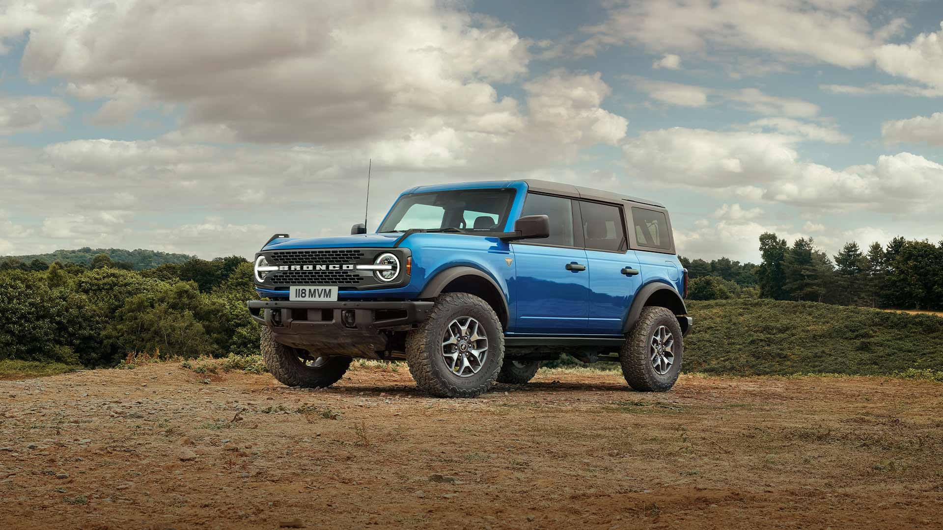 Boční pohled na modrý Ford Bronco zaparkovaný ve venkovské krajině.
