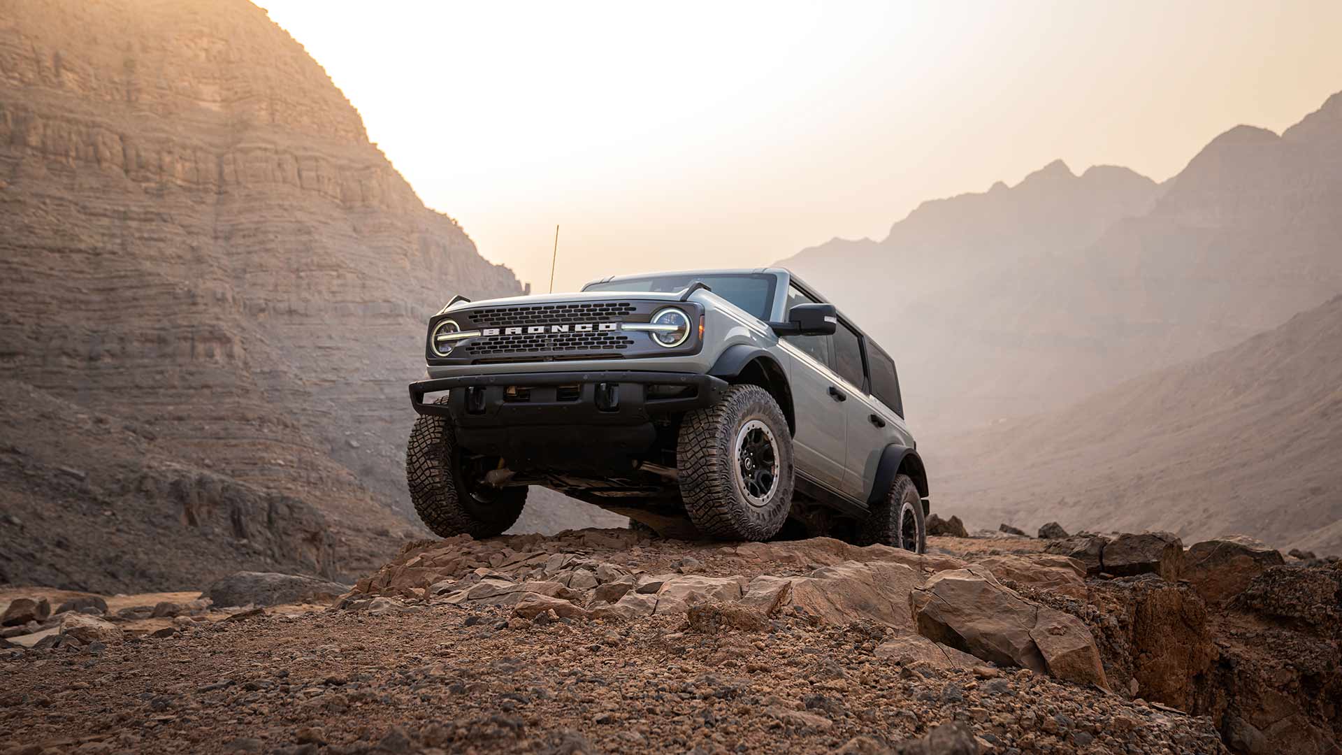 Šedý Ford Bronco stojí zaparkovaný na skalnaté cestě v horské krajině.