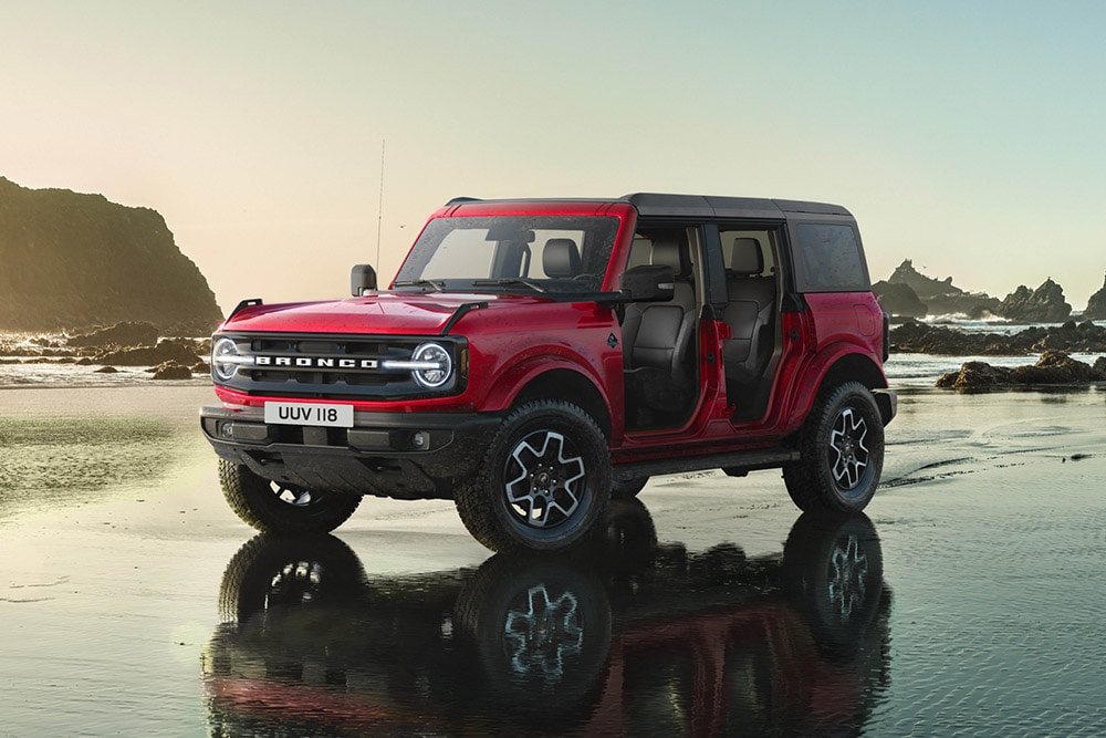 Boční pohled na šedý Ford Bronco s odstraněnými dveřmi a střechou, jak projíždí písečnou pouští.