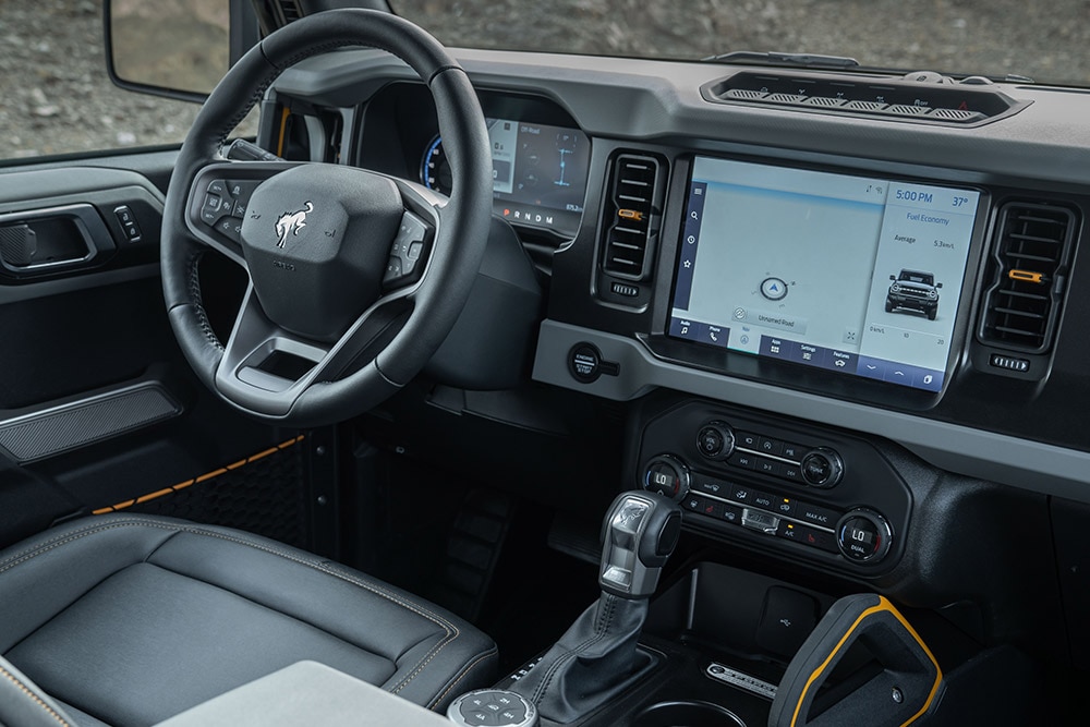 Pohled na interiér Fordu Bronco, včetně koženého volantu a připojeného touchpadu.