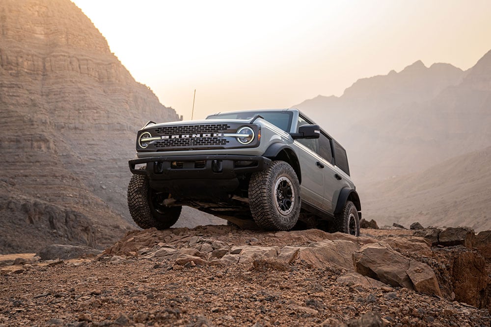 Šedý Ford Bronco stojí zaparkovaný na skalnaté cestě v horské krajině.