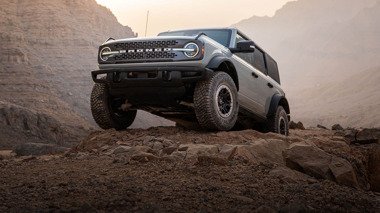 Šedý Ford Bronco stojí zaparkovaný na skalnaté cestě v horské krajině.