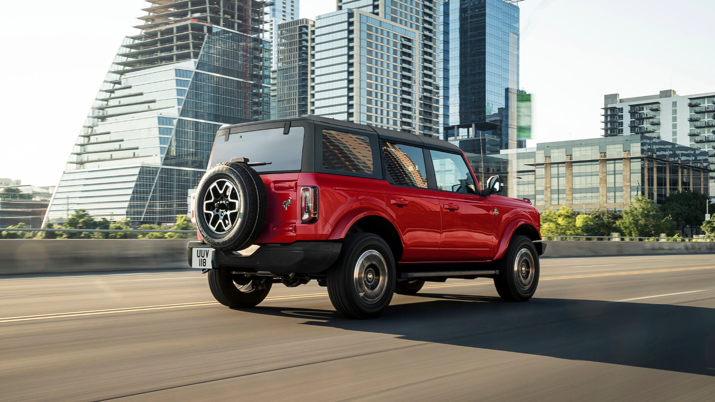 Red Ford Bronco driving on the road in front of office buildings