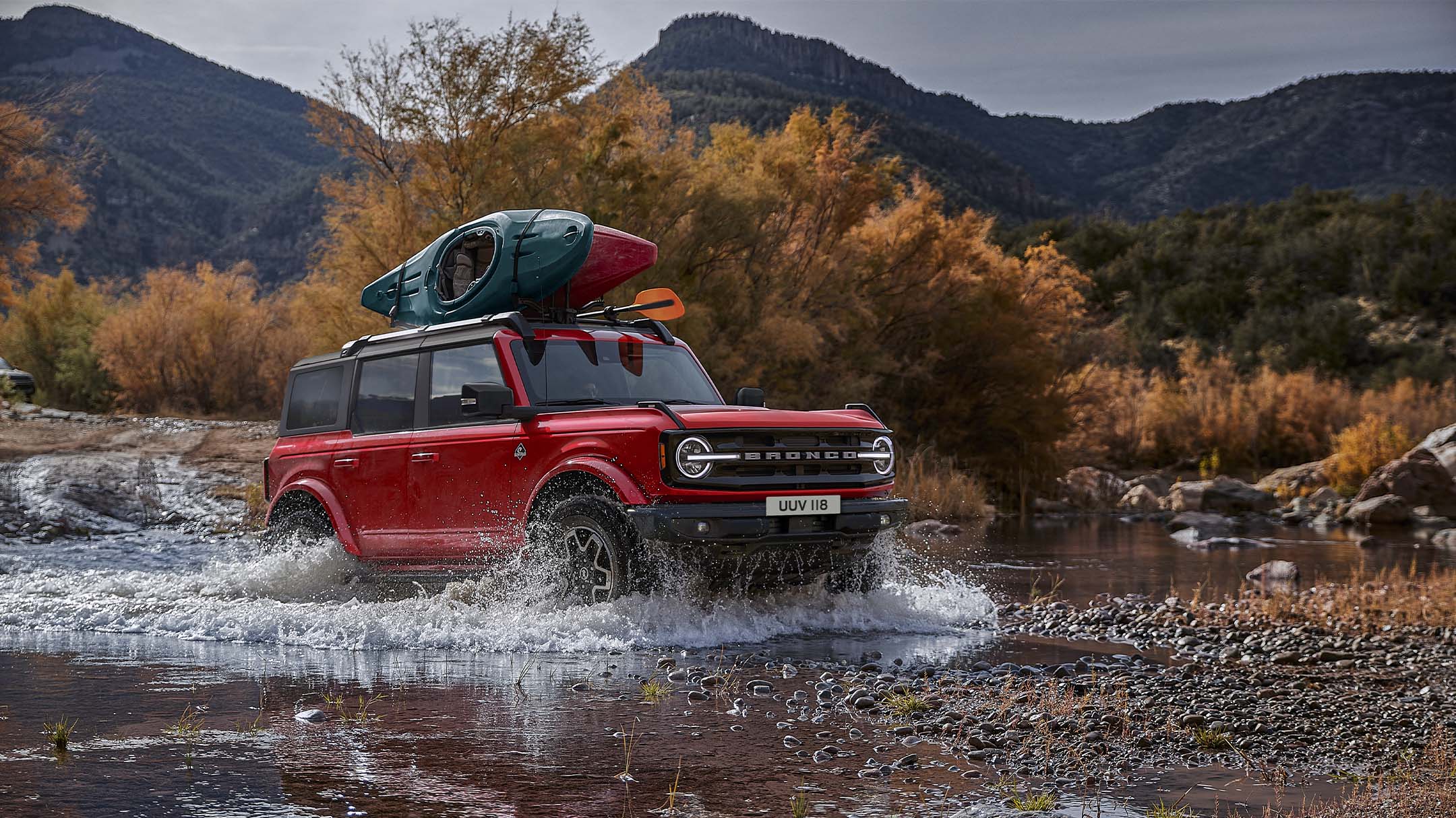 Ford Bronco driving through a small lake in the mountains with kayaks attached to the roof