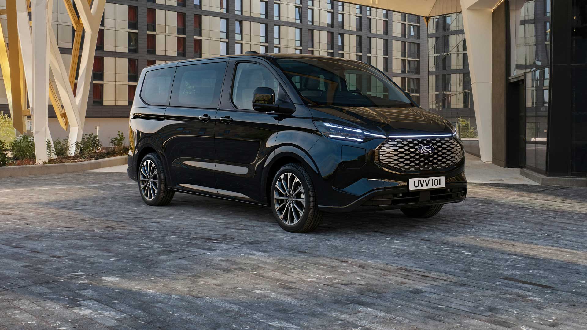 Před moderní budovou parkuje černý Ford E-Tourneo Custom.