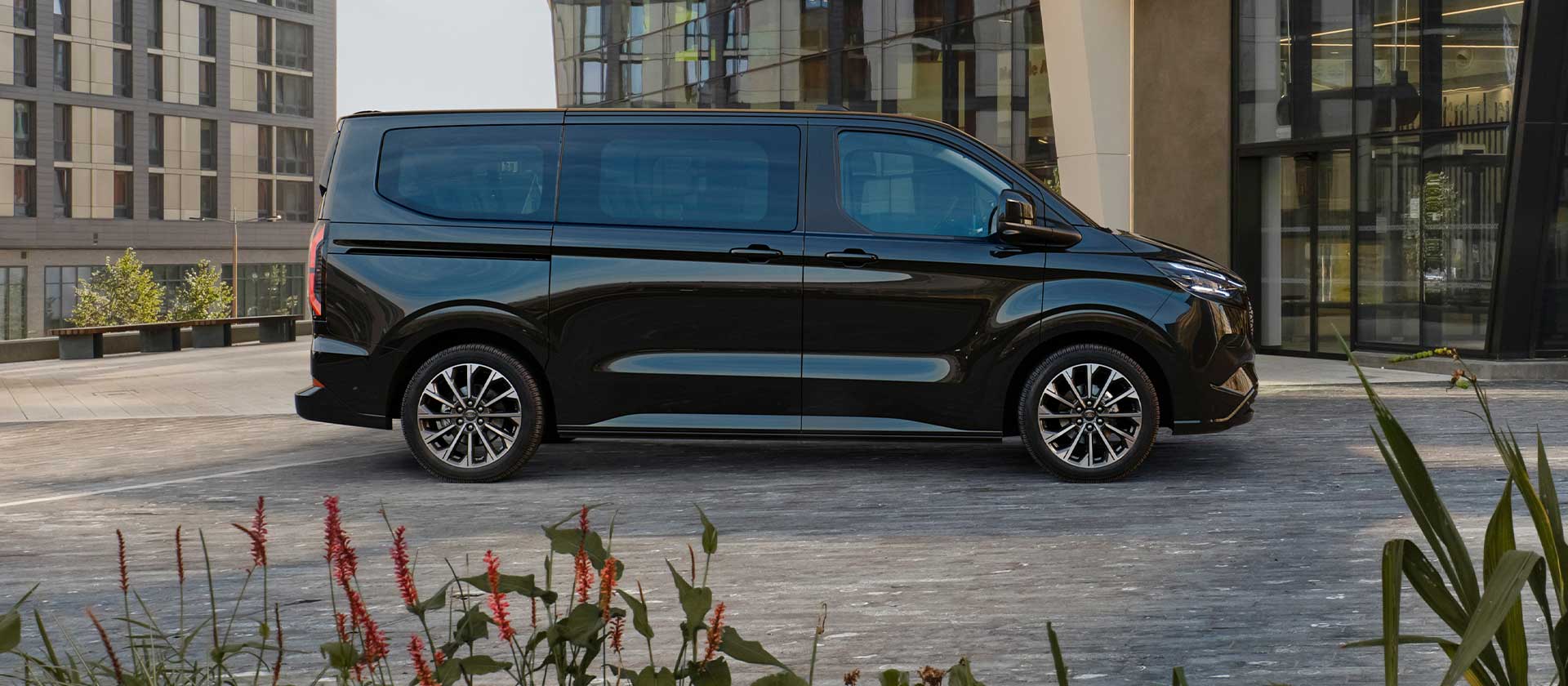 Před moderní budovou parkuje černý Ford E-Tourneo Custom.
