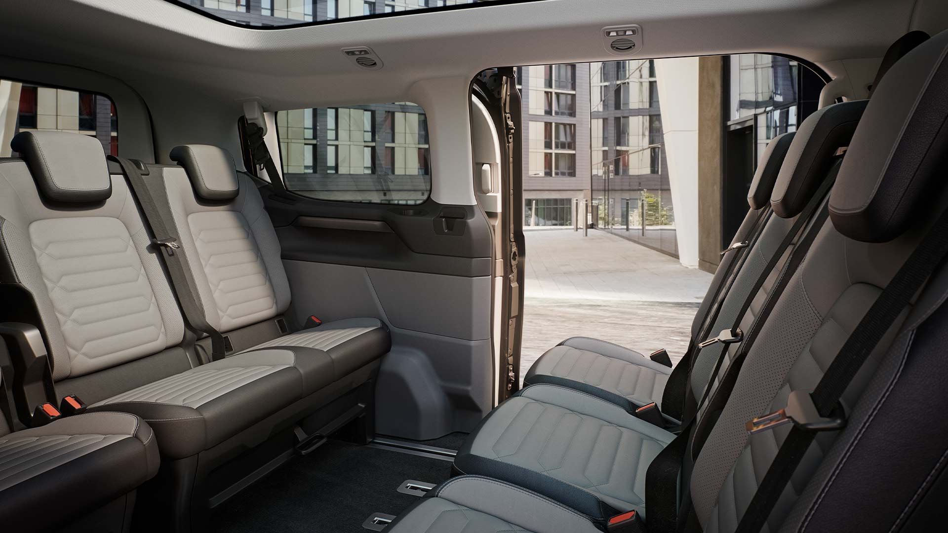 Pohled do interiéru vozu Ford Tourneo Custom na zadní řady sedadel a panoramatickou střechu.