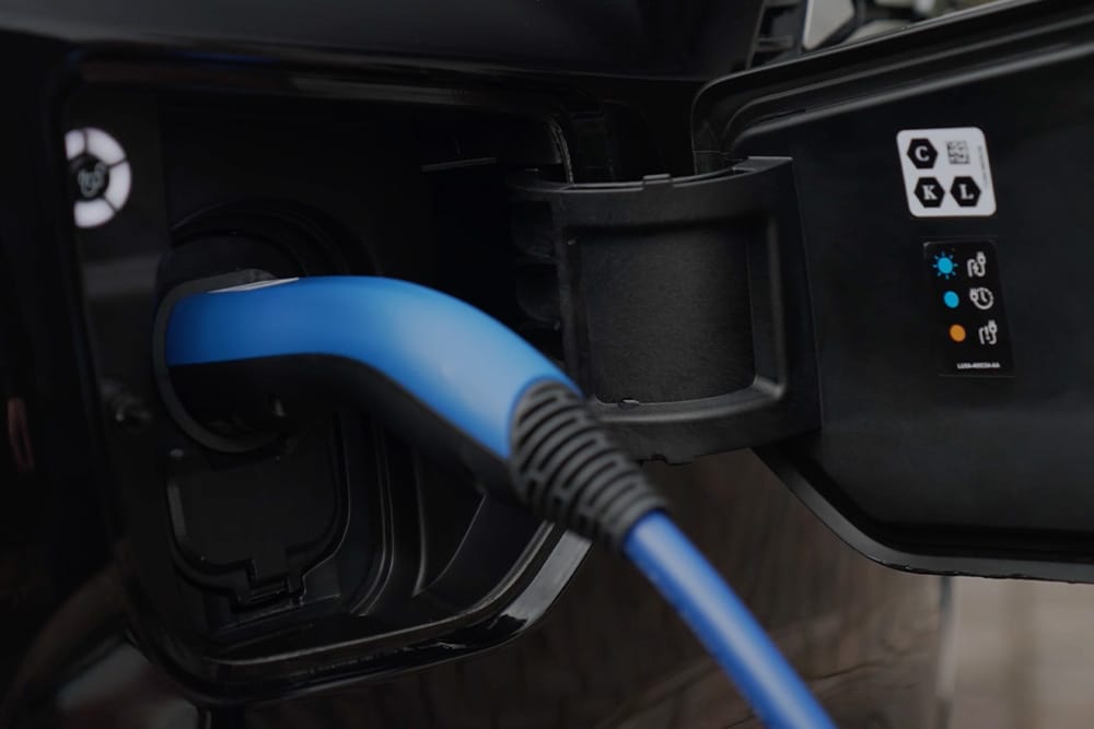 Detail modrého nabíjecího kabelu zapojeného do nabíjecího portu elektrického vozidla.