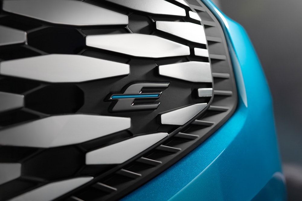 Detail masky vozu Ford E-Tourneo Custom s modrým logem „E“ elektrických vozidel Ford.