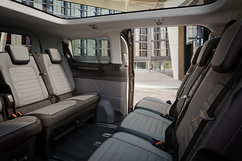 Pohled do interiéru vozu Ford Tourneo Custom na zadní řady sedadel a panoramatickou střechu.