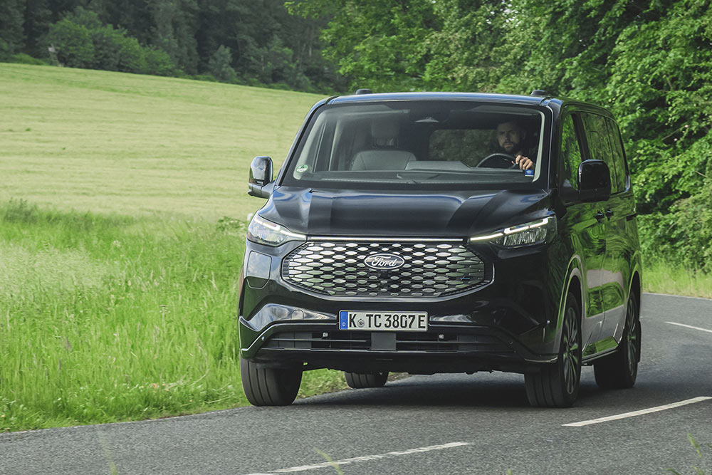 Černý Ford E-Tourneo Custom jedoucí po silnici mezi městy.