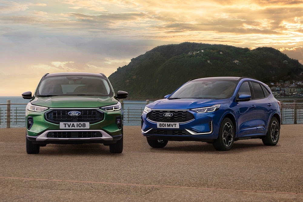 A green Ford Kuga Active and a blue Ford Kuga ST Line parked side-by-side in a coastal car park. 