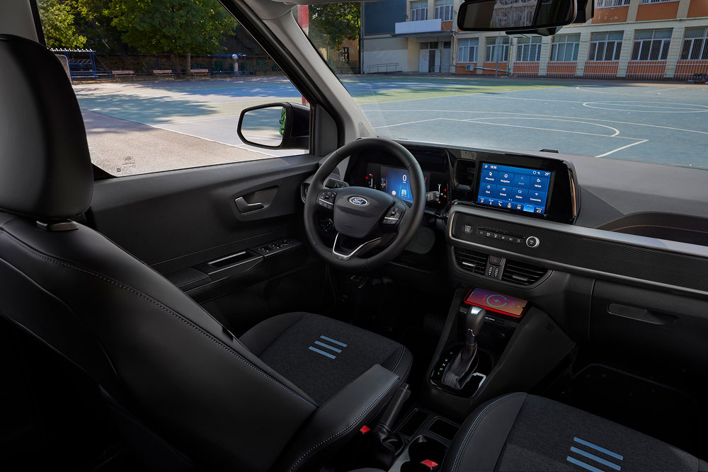 Interiér Fordu Tourneo Courier zobrazující palubní desku, volant, obrazovku infotainmentu a přední sedadlo spolujezdce.