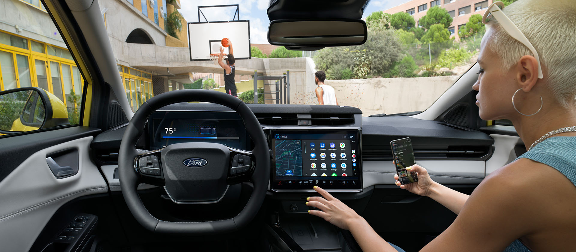 Člověk v interiéru elektrického Fordu Puma Gen-E ® bezdrátově synchronizuje mobilní telefon přes velkou dotykovou obrazovkou vozu.