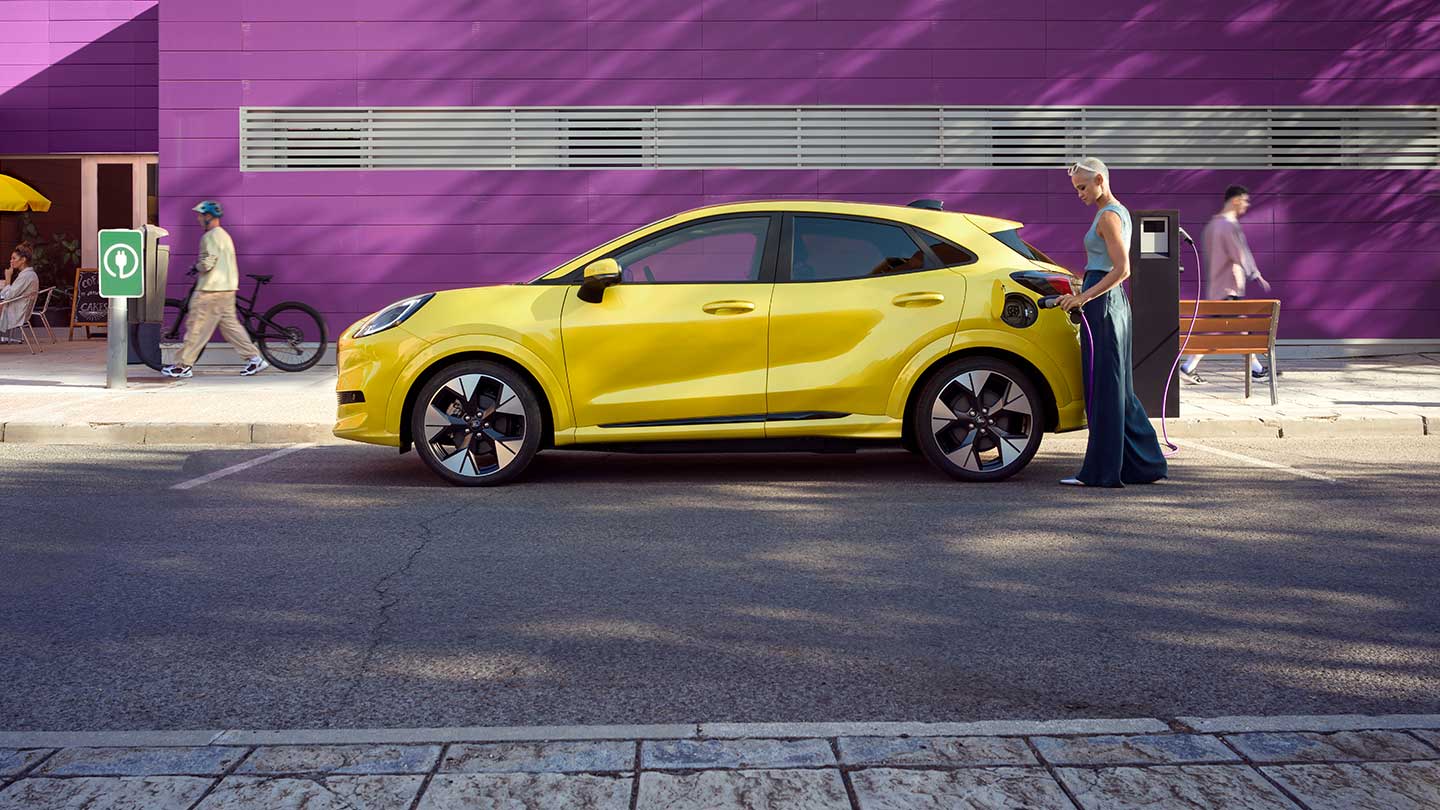Boční pohled na žlutý elektrický Ford Puma Gen-E® připojený k veřejné nabíjecí stanici na parkovacím místě.