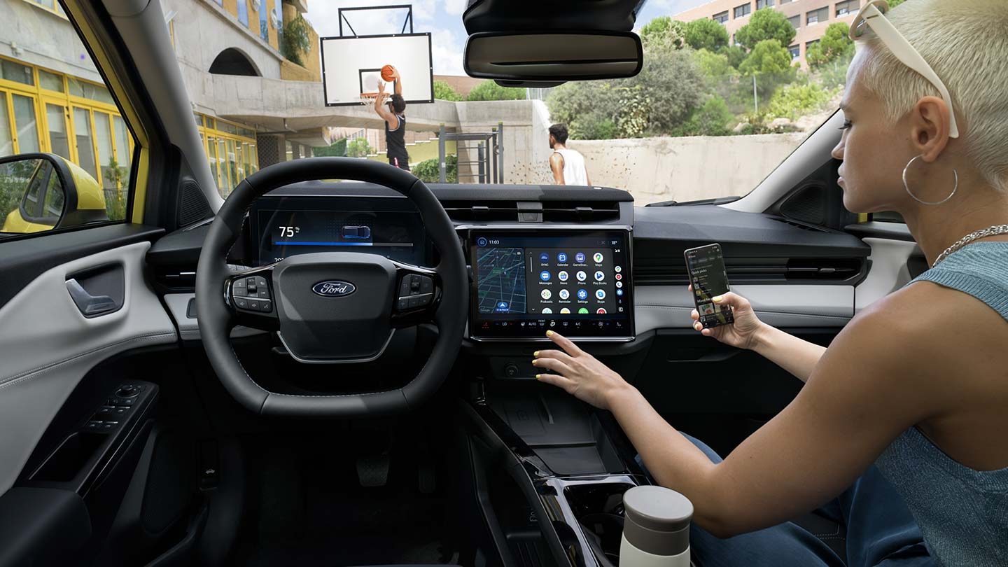 Člověk v interiéru elektrického Fordu Puma Gen-E ® bezdrátově synchronizuje mobilní telefon přes velkou dotykovou obrazovkou vozu.