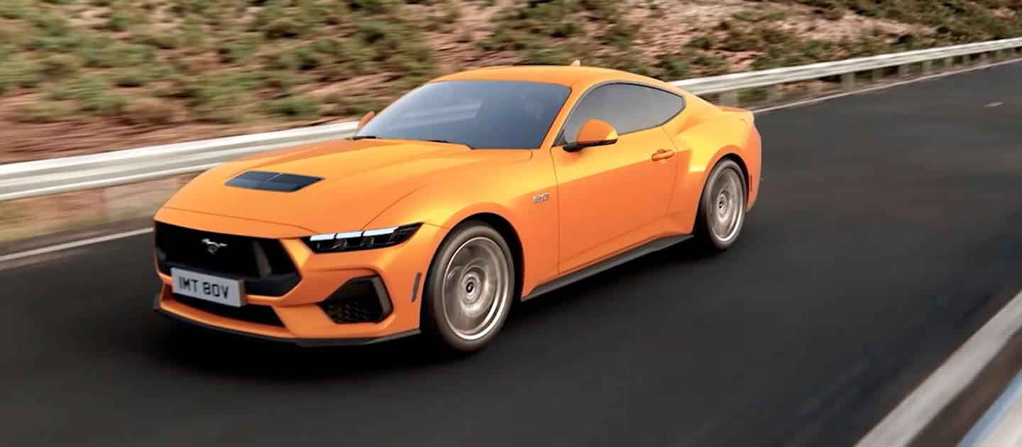 Ford Mustang GT Fastback v barvě Orange Fury jedoucí po horské silnici