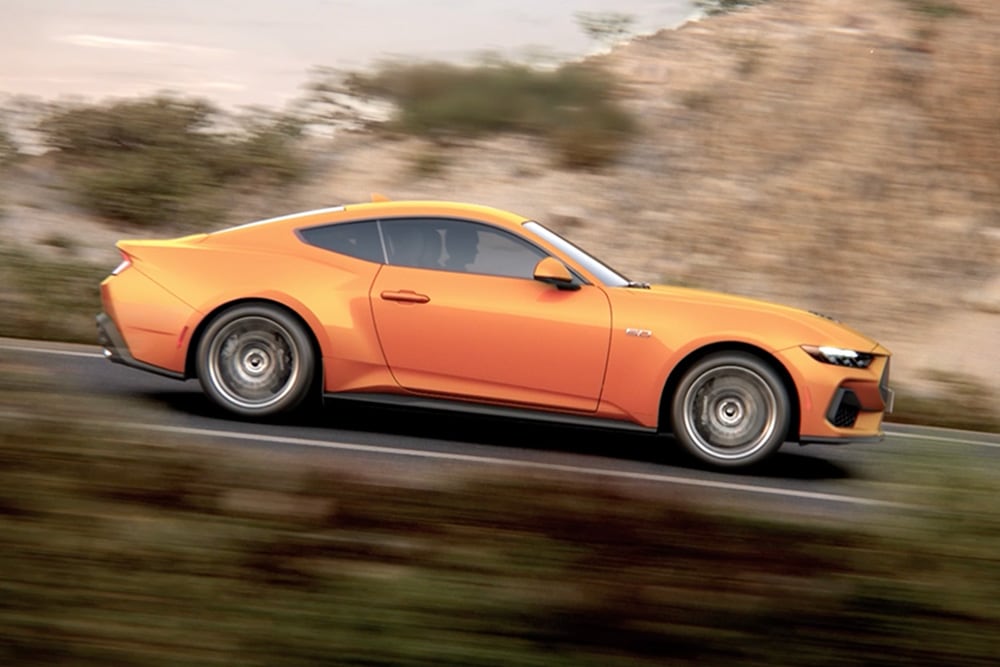 Boční pohled na Ford Mustang GT Fastback v barvě Orange Fury jedoucí po silnici