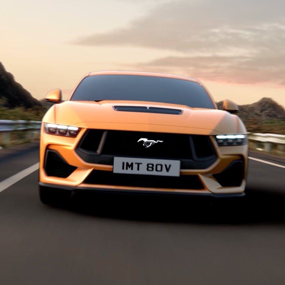 Přední pohled na oranžový Ford Mustang s detailním záběrem na světlomety, masku chladiče a znak Mustang