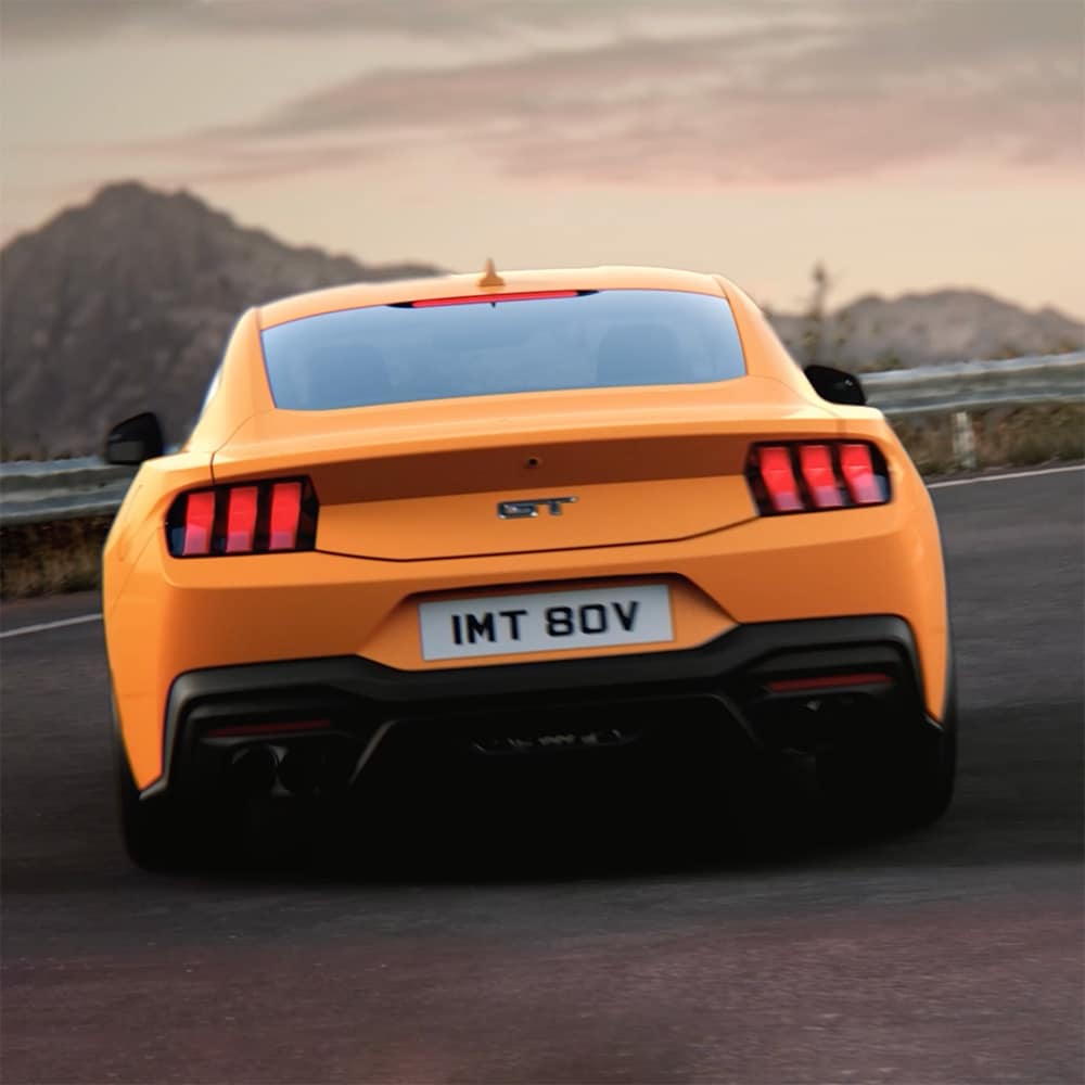 Zadní část Ford Mustang GT Fastback v barvě Orange Fury projíždějící ostrou zatáčku na venkovské silnici