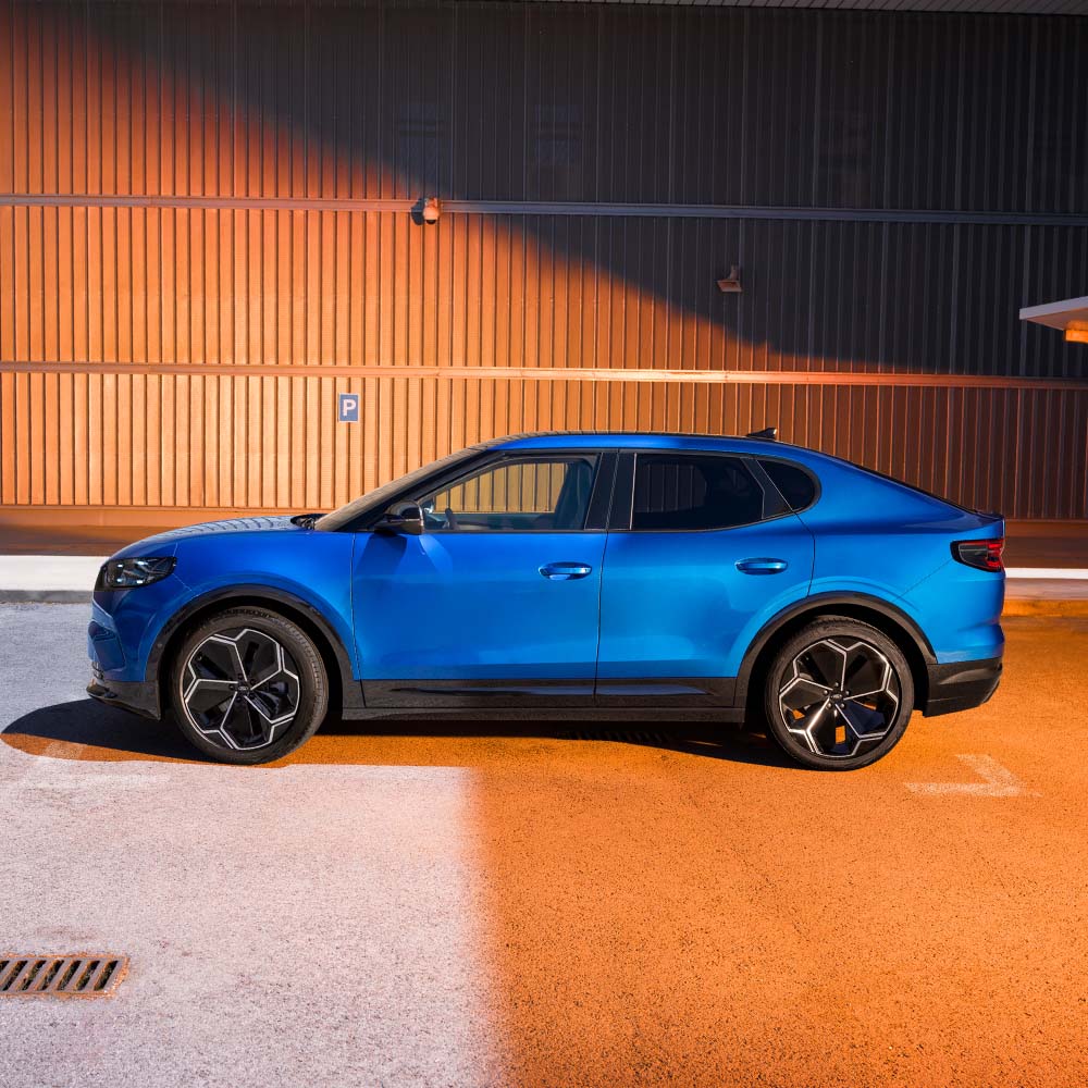 A side view of a blue Ford Capri parked in front of a textured wall.