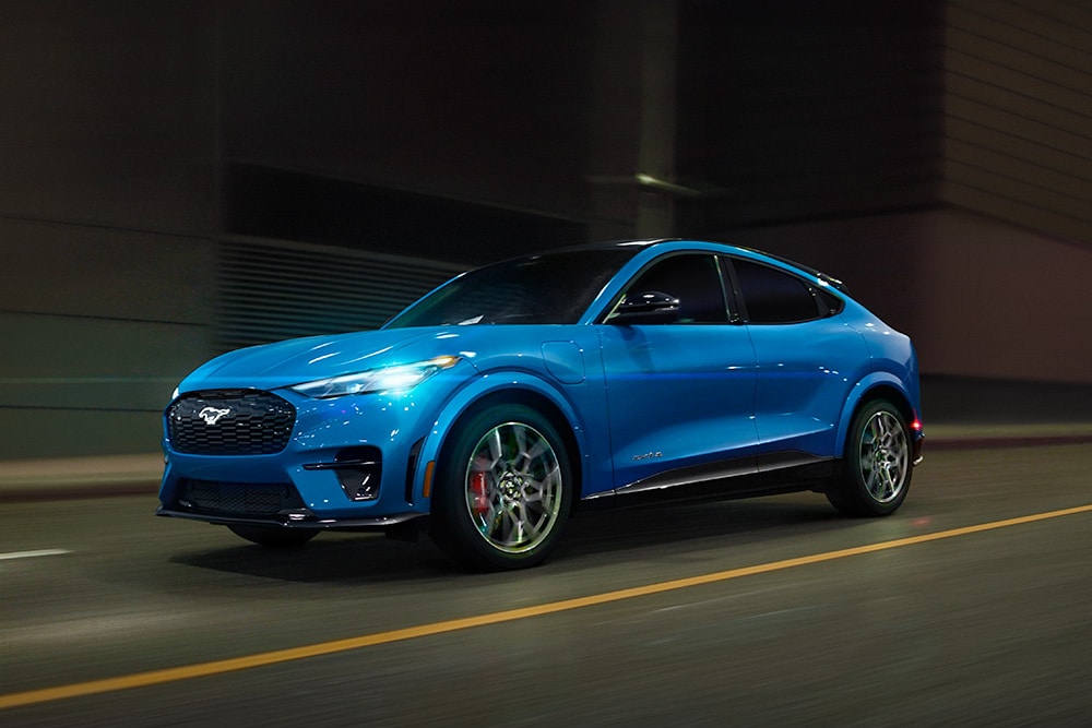 Modrý elektrický sportovní vůz Ford Mustang Mach-E GT jedoucí po otevřené silnici.