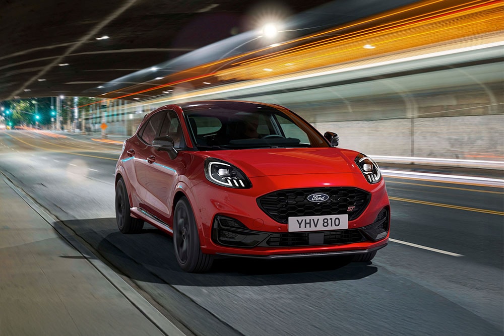 Červené sportovní SUV Ford Puma ST jedoucí v noci po jasně osvětlené městské silnici.