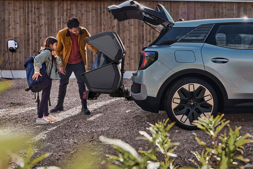 Muž a dítě stojí u otevřeného zavazadlového prostoru SUV Ford Explorer a nakládají složený kočárek.